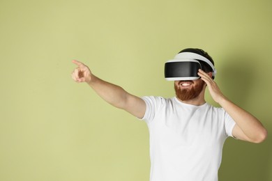 Photo of Smiling man using virtual reality headset on pale green background. Space for text