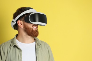Photo of Smiling man using virtual reality headset on pale yellow background. Space for text