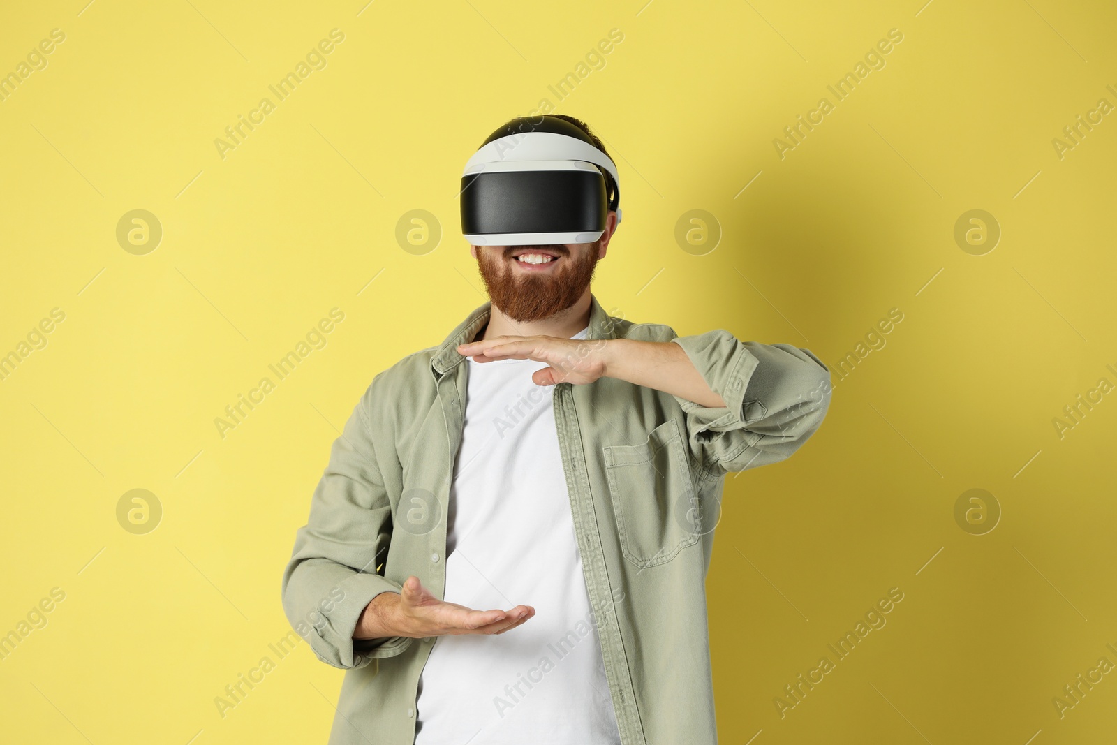 Photo of Happy man using virtual reality headset on pale yellow background