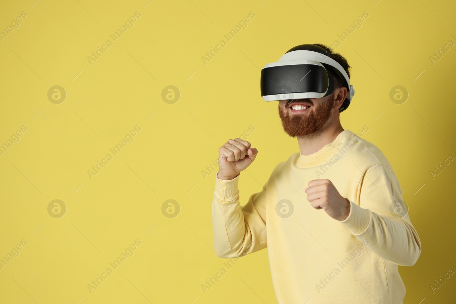 Photo of Happy man using virtual reality headset on pale yellow background. Space for text