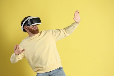 Photo of Happy man using virtual reality headset on pale yellow background. Space for text