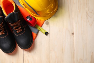 Photo of Pair of working boots, hard hat and tape measure on wooden surface, top view. Space for text