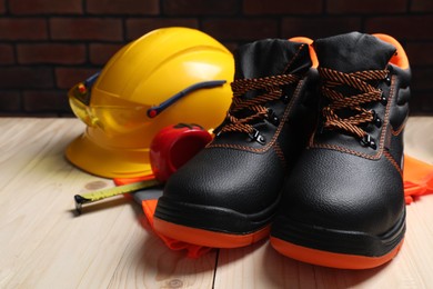 Photo of Pair of working boots, hard hat and tape measure on wooden surface