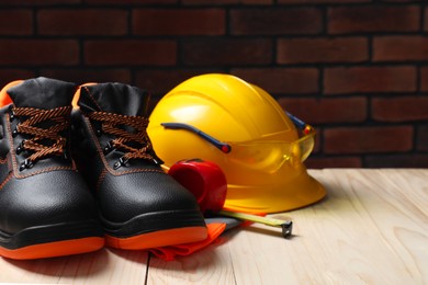 Photo of Pair of working boots, hard hat and tape measure on wooden surface. Space for text