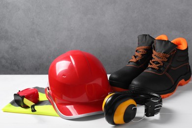 Photo of Pair of working boots, hard hat, tape measure, reflective vest and earmuffs on white surface