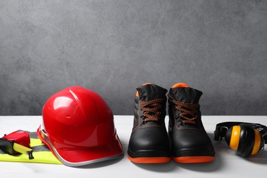 Photo of Pair of working boots, hard hat, tape measure, reflective vest and earmuffs on white surface