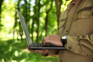 Forester with laptop examining plants in forest, closeup