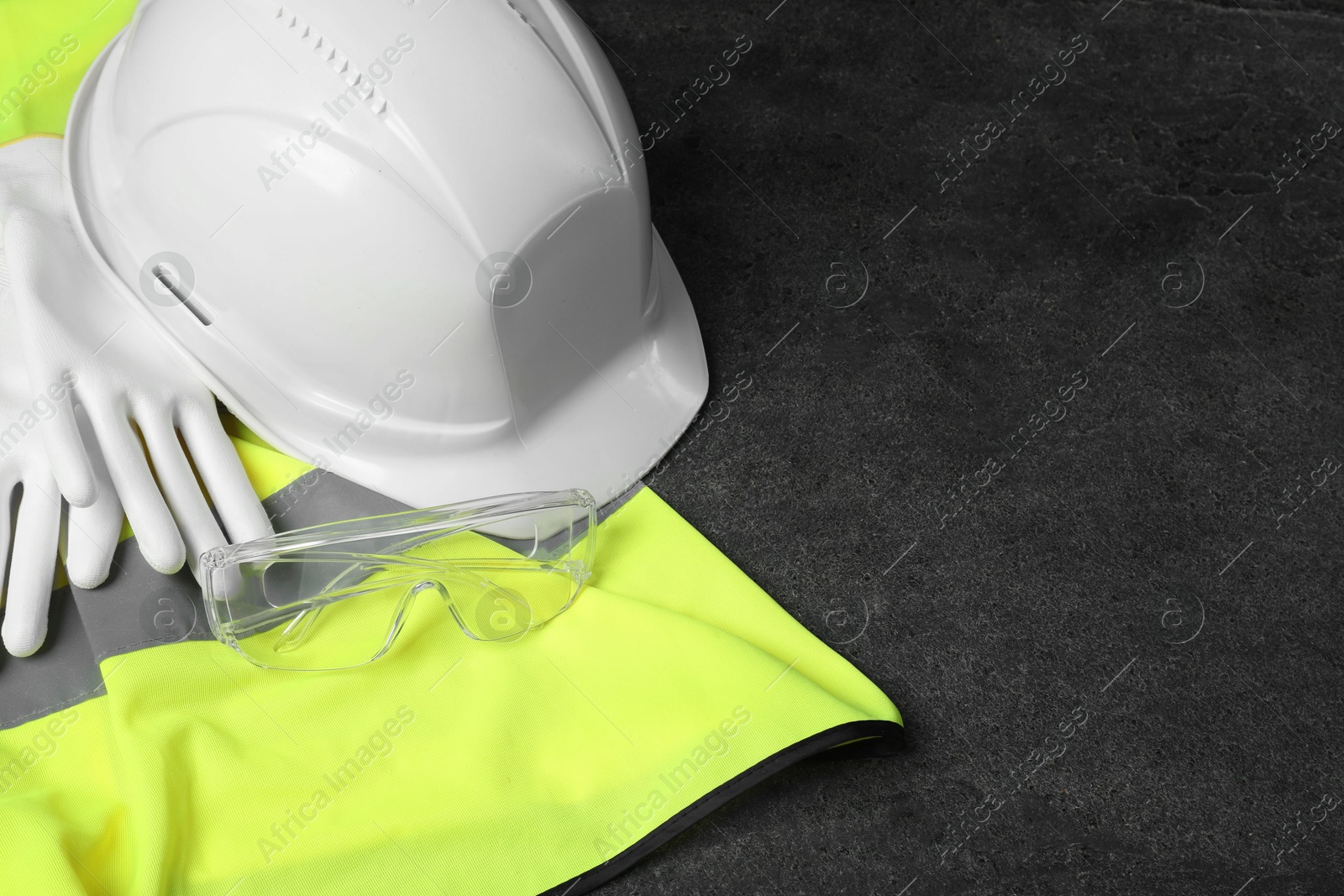 Photo of Reflective vest, hard hat, protective gloves and goggles on gray background, closeup. Space for text
