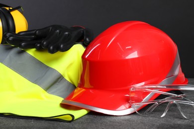 Photo of Reflective vest, hard hat, earmuffs, protective gloves and goggles on gray surface, closeup