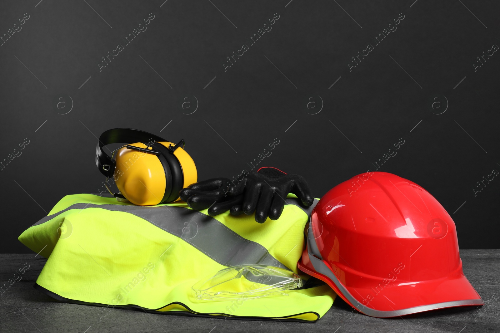 Photo of Reflective vest, hard hat, earmuffs, protective gloves and goggles on gray surface, space for text