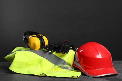 Photo of Reflective vest, hard hat, earmuffs, protective gloves and goggles on gray surface, space for text