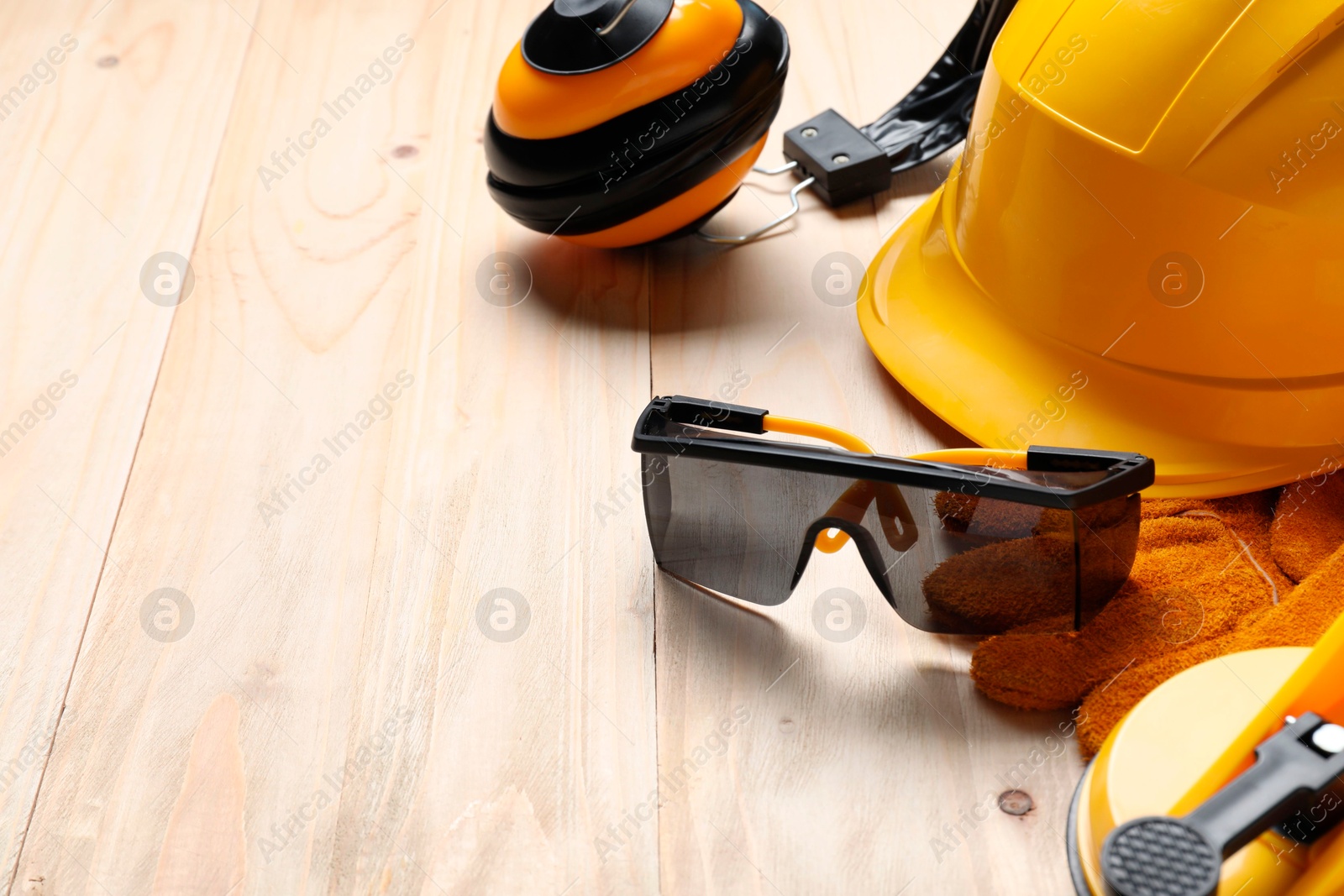 Photo of Hard hat, goggles, protective glove, earmuffs on wooden background, space for text