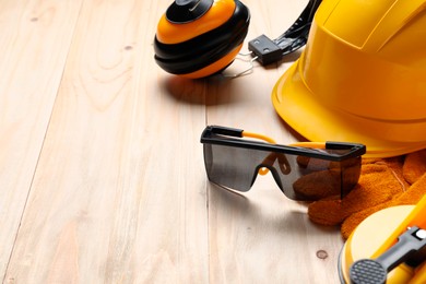 Photo of Hard hat, goggles, protective glove, earmuffs on wooden background, space for text