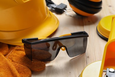 Photo of Hard hat, goggles, protective gloves, earmuffs and suction lifters on wooden background, closeup