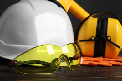 Photo of Hard hat, earmuffs, goggles and protective gloves on wooden surface, closeup