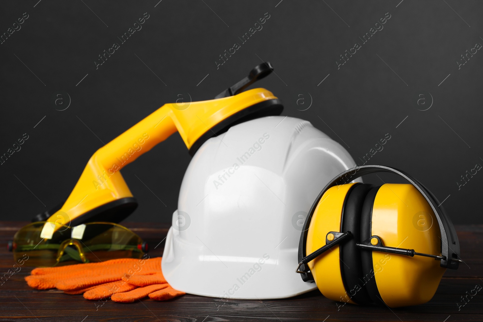 Photo of Hard hat, earmuffs, suction lifters and protective gloves on wooden surface against gray background