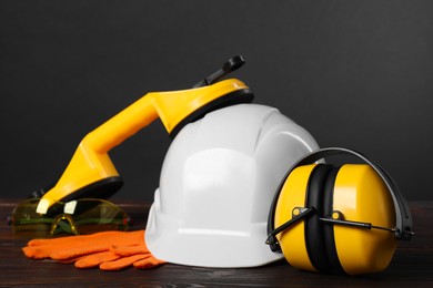 Photo of Hard hat, earmuffs, suction lifters and protective gloves on wooden surface against gray background