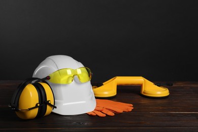 Photo of Hard hat, goggles, earmuffs, suction lifters and protective gloves on wooden surface against gray background, space for text