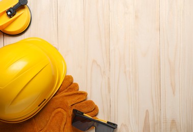 Photo of Hard hat, protective gloves, earmuffs and goggles on wooden background, flat lay. Space for text