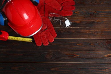 Photo of Hard hat, earmuffs, protective gloves and tape measure on wooden background, flat lay. Space for text
