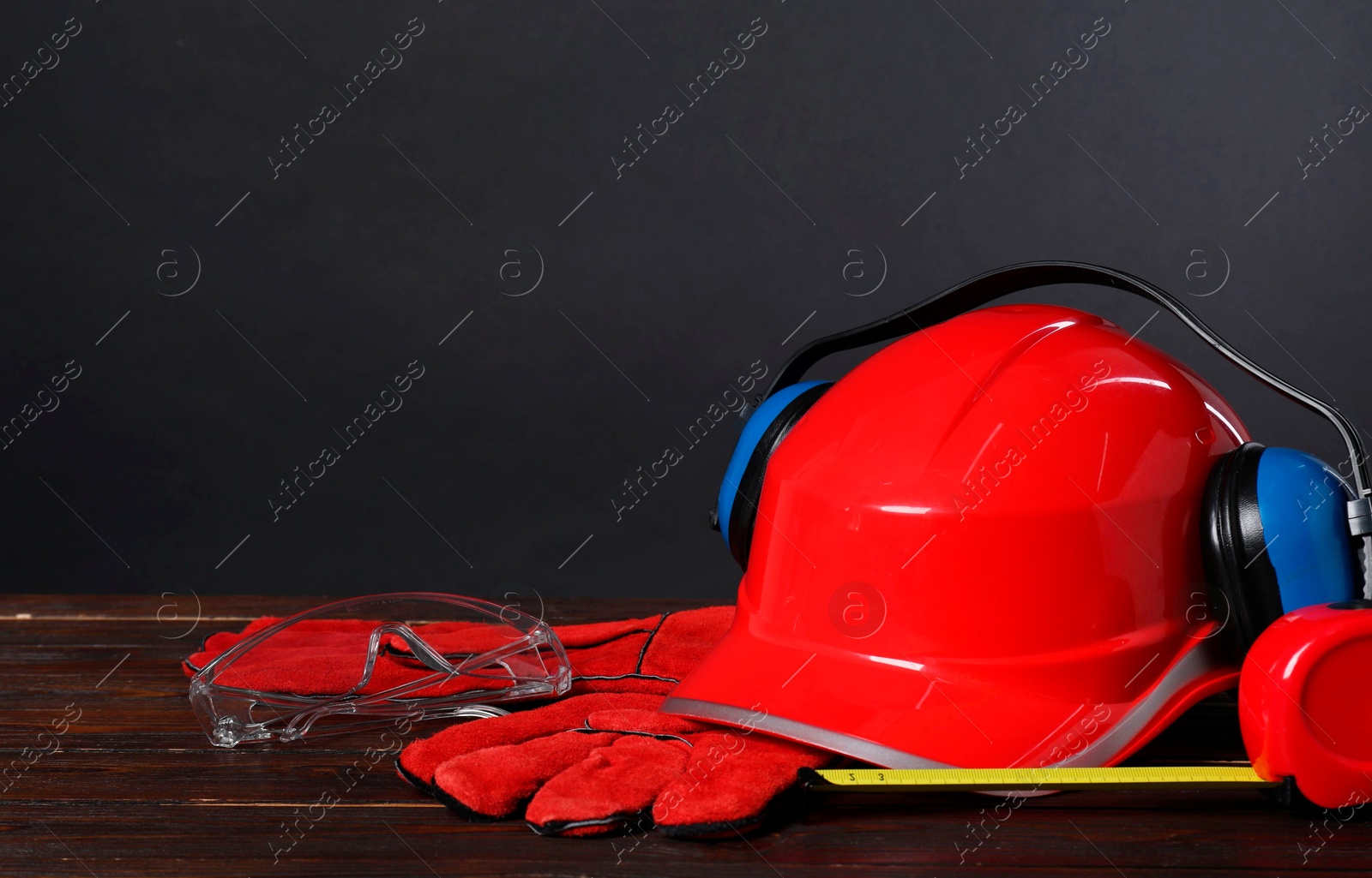 Photo of Hard hat, earmuffs, protective gloves and tape measure on wooden surface against gray background, space for text