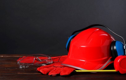 Photo of Hard hat, earmuffs, protective gloves and tape measure on wooden surface against gray background, space for text