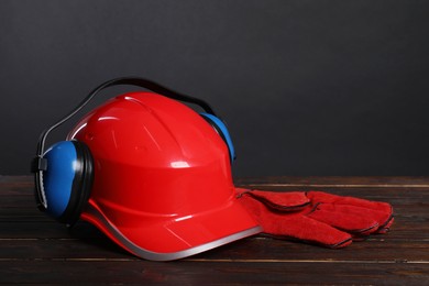 Photo of Hard hat, earmuffs and protective gloves on wooden surface against gray background,, space for text