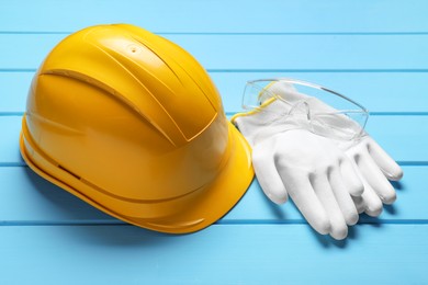 Photo of Hard hat, protective gloves and goggles on light blue wooden background