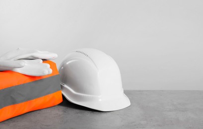 Photo of Reflective vest, hard hat and protective gloves on gray surface against light background, space for text
