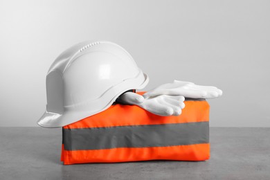 Photo of Reflective vest, hard hat and protective gloves on gray surface against light background