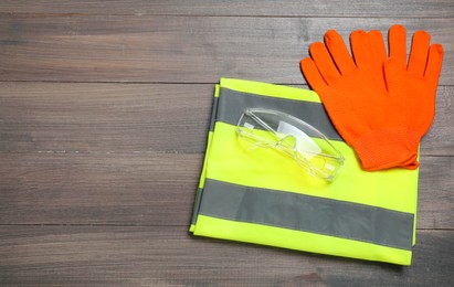 Photo of Reflective vest, protective gloves and goggles on wooden background, top view. Space for text