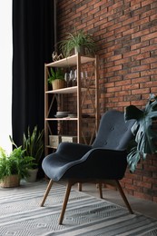 Shelving unit, green houseplants, armchair and elegant curtain in room. Interior design