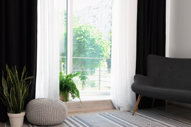 Photo of Sofa, green houseplants, pouffe and elegant curtains in room. Interior design