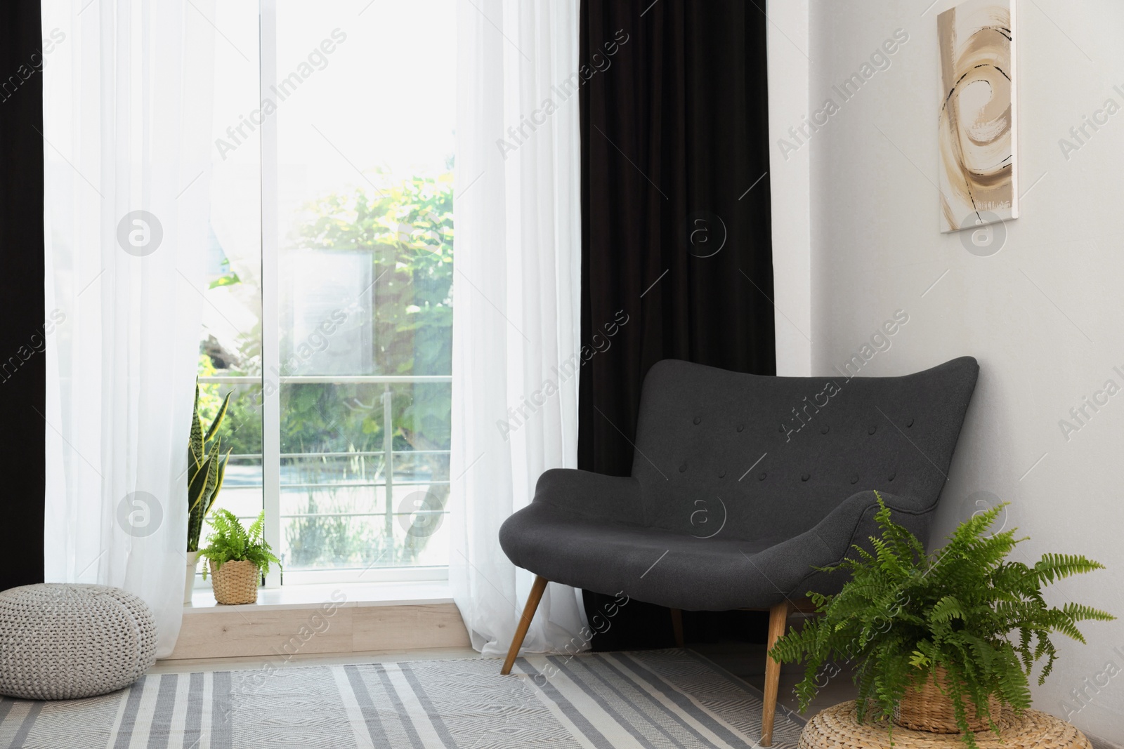 Photo of Sofa, green houseplants, pouffe and elegant curtains in room. Interior design