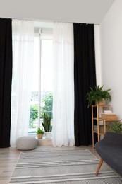 Photo of Shelving unit, sofa, green houseplants, pouffe and elegant curtains in room. Interior design