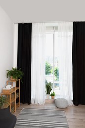 Photo of Shelving unit, green houseplants, pouffe and elegant curtains in room. Interior design