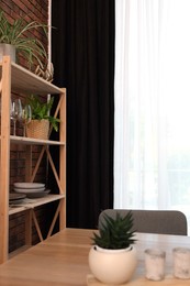 Photo of Shelving unit, table, chair and elegant curtain in room. Interior design