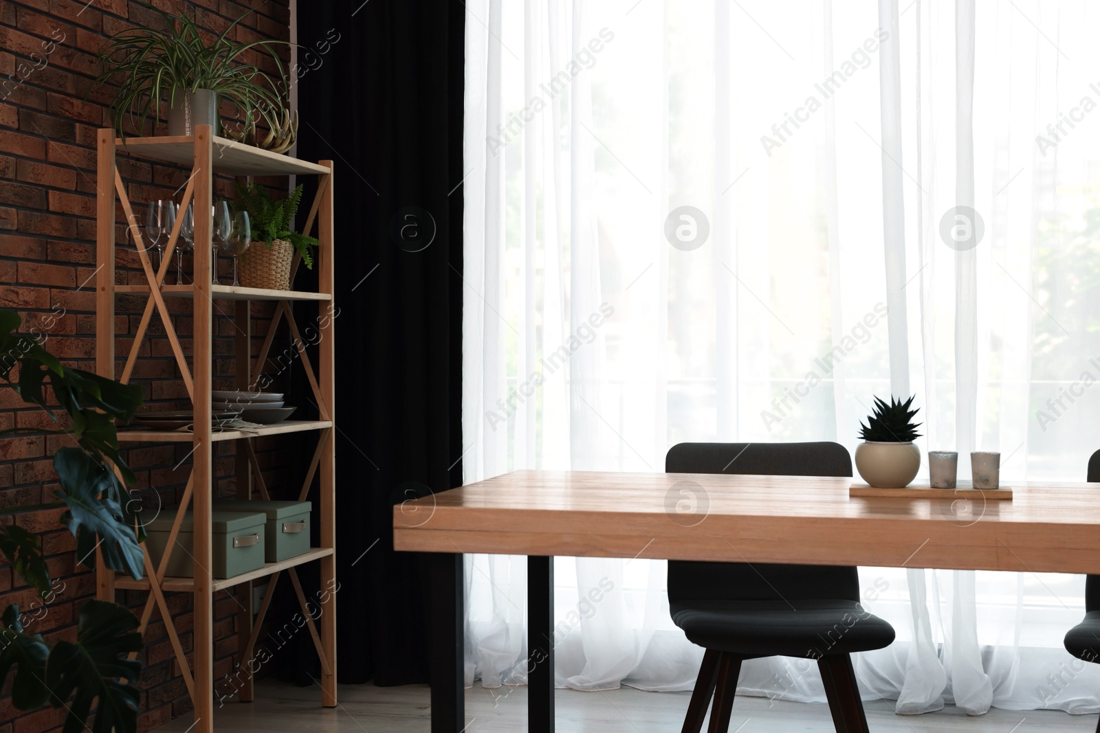 Photo of Shelving unit, table, chair, green houseplants and elegant curtain in room. Interior design