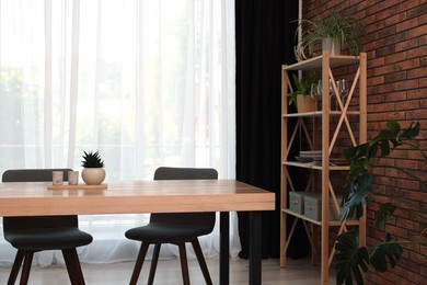 Photo of Shelving unit, table, chairs, green houseplants and elegant curtain in room. Interior design