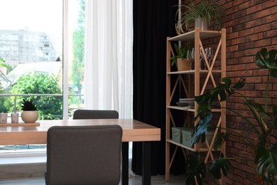 Photo of Shelving unit, table, chairs, green houseplants and elegant curtain in room. Interior design