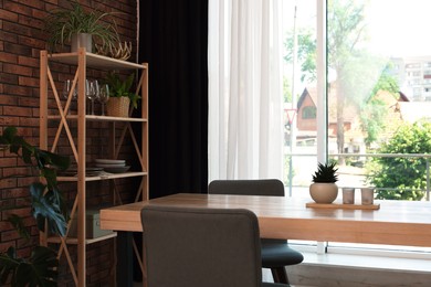 Photo of Shelving unit, table, chairs, green houseplants and elegant curtain in room. Interior design