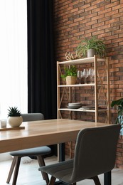 Shelving unit, table, chairs, green houseplants and elegant curtain in room. Interior design