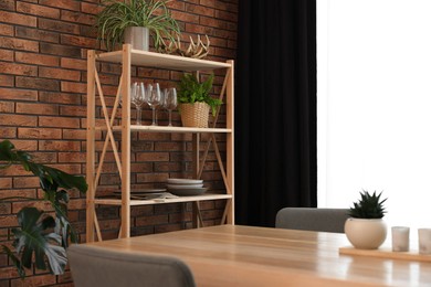 Photo of Shelving unit, table, chairs, green houseplants and elegant curtain in room. Interior design