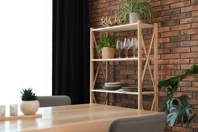 Photo of Shelving unit, table, chairs, green houseplants and elegant curtain in room. Interior design