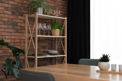 Photo of Shelving unit, table, chairs, green houseplants and elegant curtain in room. Interior design