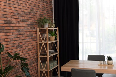 Shelving unit, table, chairs, green houseplants and elegant curtain in room. Interior design