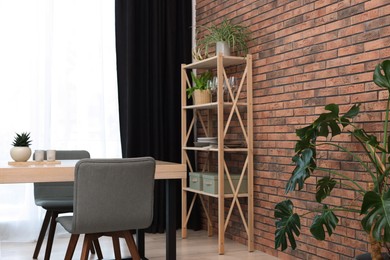 Shelving unit, table, chairs, green houseplants and elegant curtain in room. Interior design