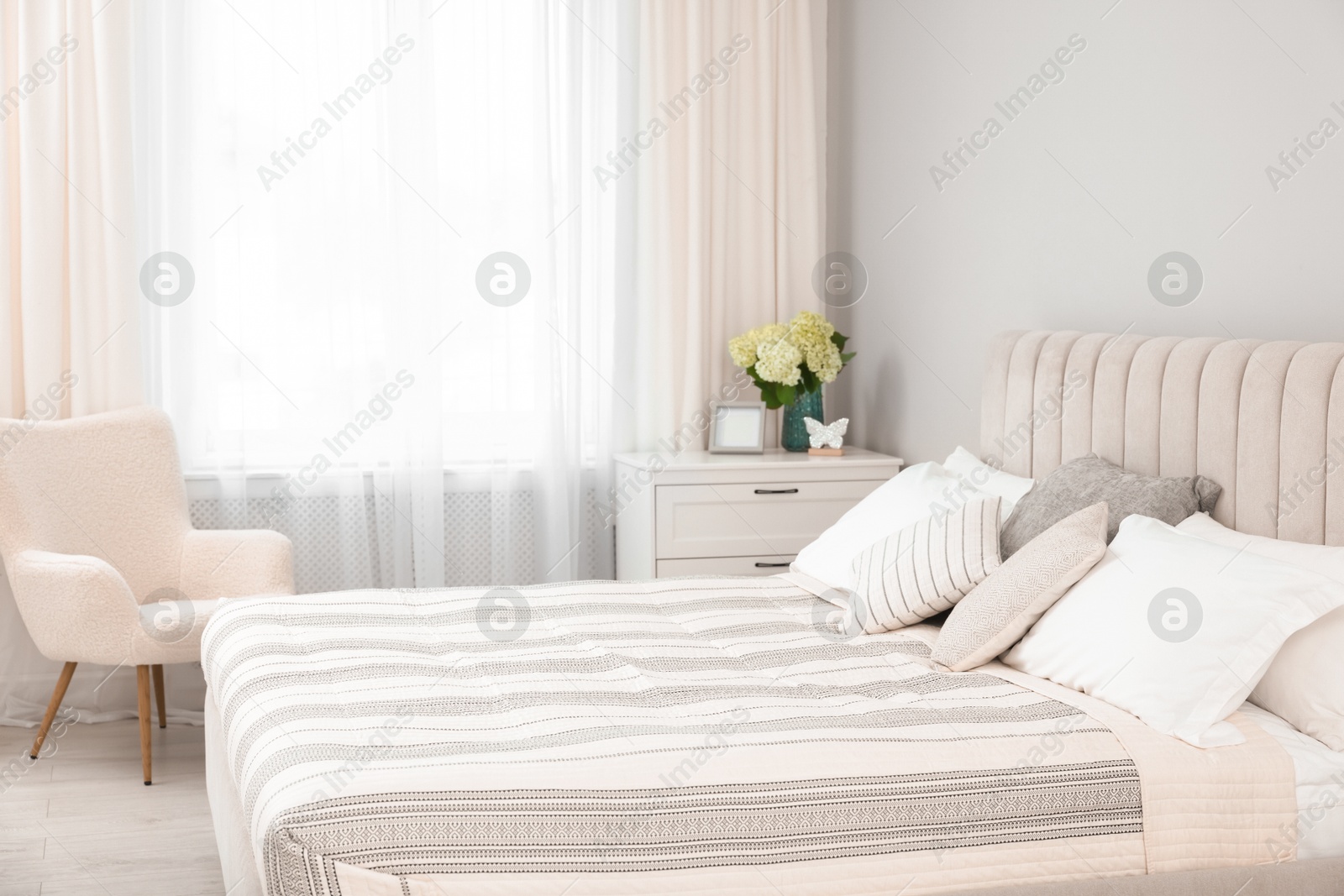 Photo of Large bed, chest of drawers, armchair and window with curtains in bedroom. Interior design