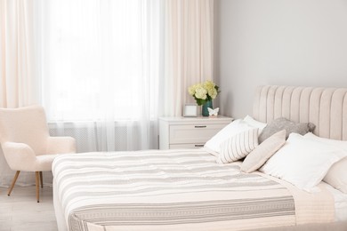 Photo of Large bed, chest of drawers, armchair and window with curtains in bedroom. Interior design