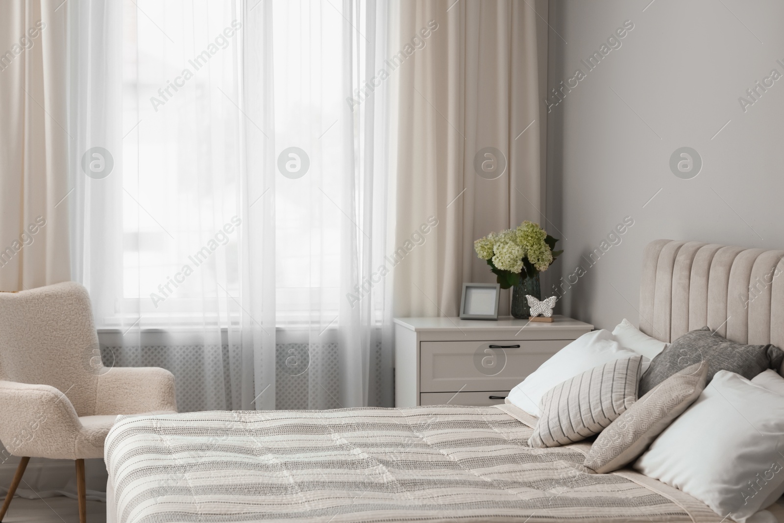 Photo of Large bed, chest of drawers, armchair and window with curtains in bedroom. Interior design